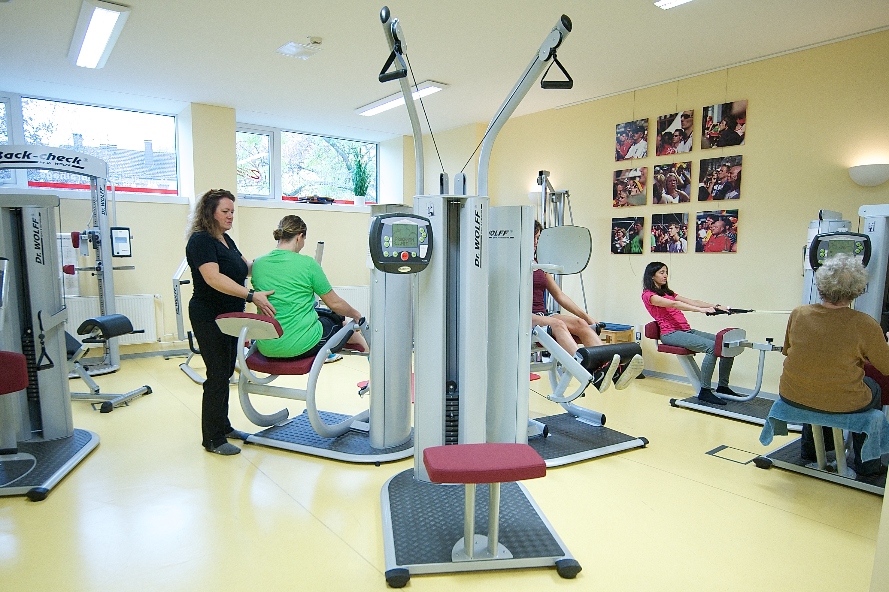 Einblick in einen Fitnessraum mit trainierenden Menschen und einer Physiotherapeutin